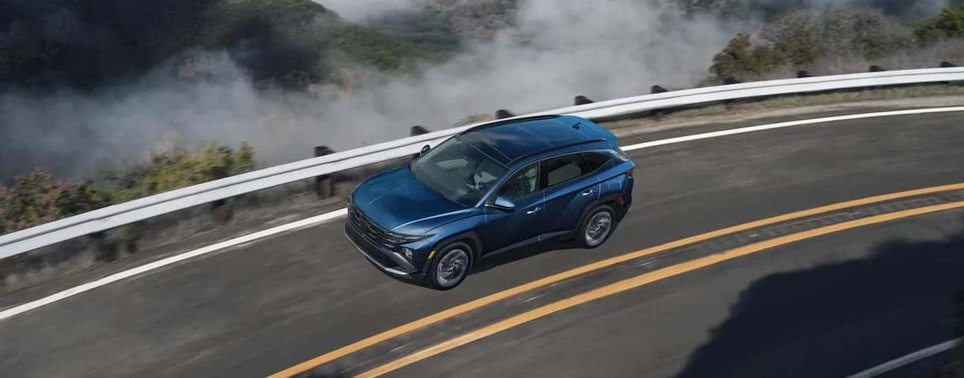 A blue 2025 Hyundai Tucson driving on a highway.