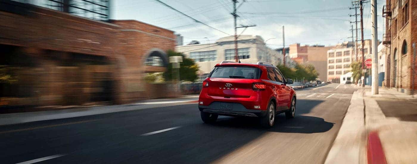 Rear of a red 2026 Hyundai Venue driving down a road.