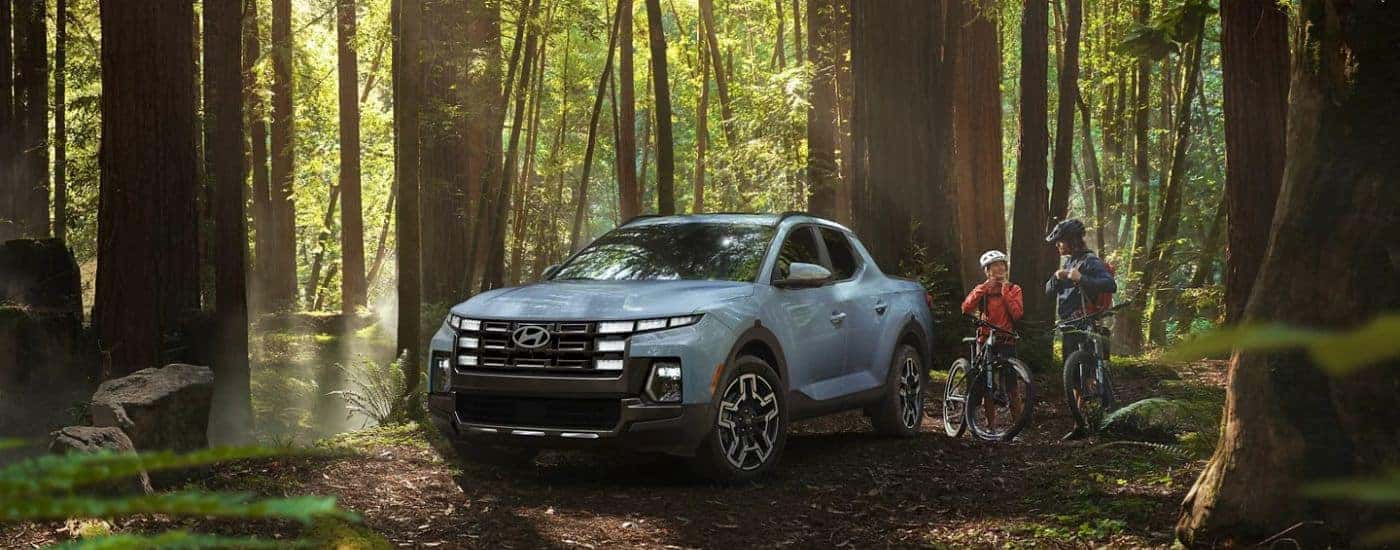 A blue 2026 Hyundai Santa Cruz Limited parked in woods by two bicyclists.