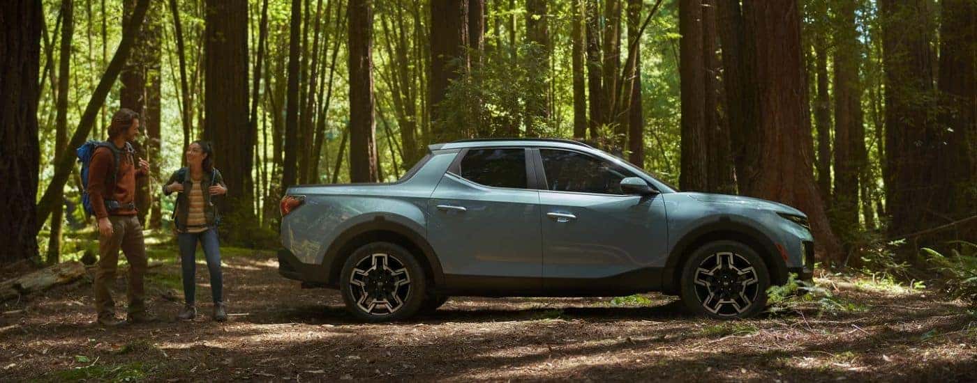 A blue 2026 Hyundai Santa Cruz Limited shown parked in the woods next to a couple.