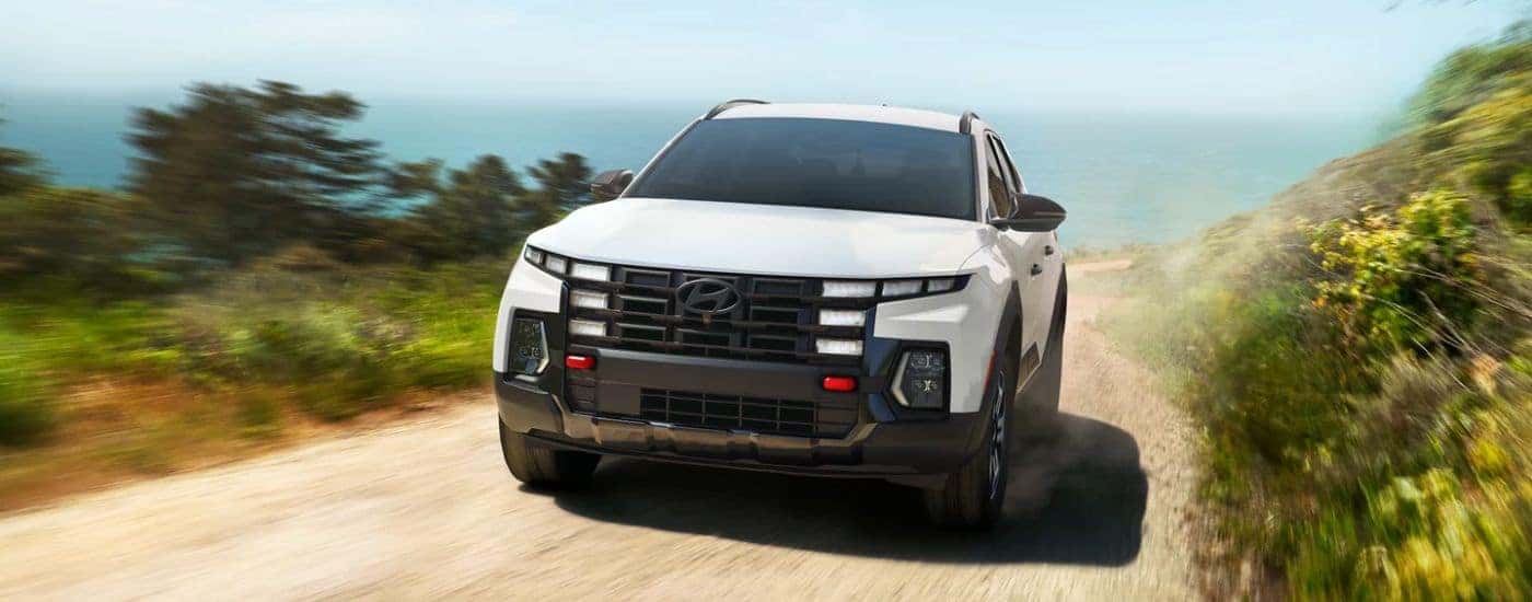 A white 2026 Hyundai Santa Cruz shown driving a beach road.