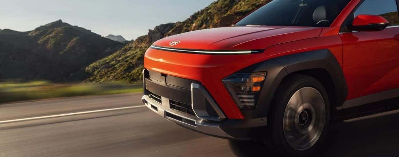 Front end of an orange 2024 Hyundai Kona Limited driving a paved road.