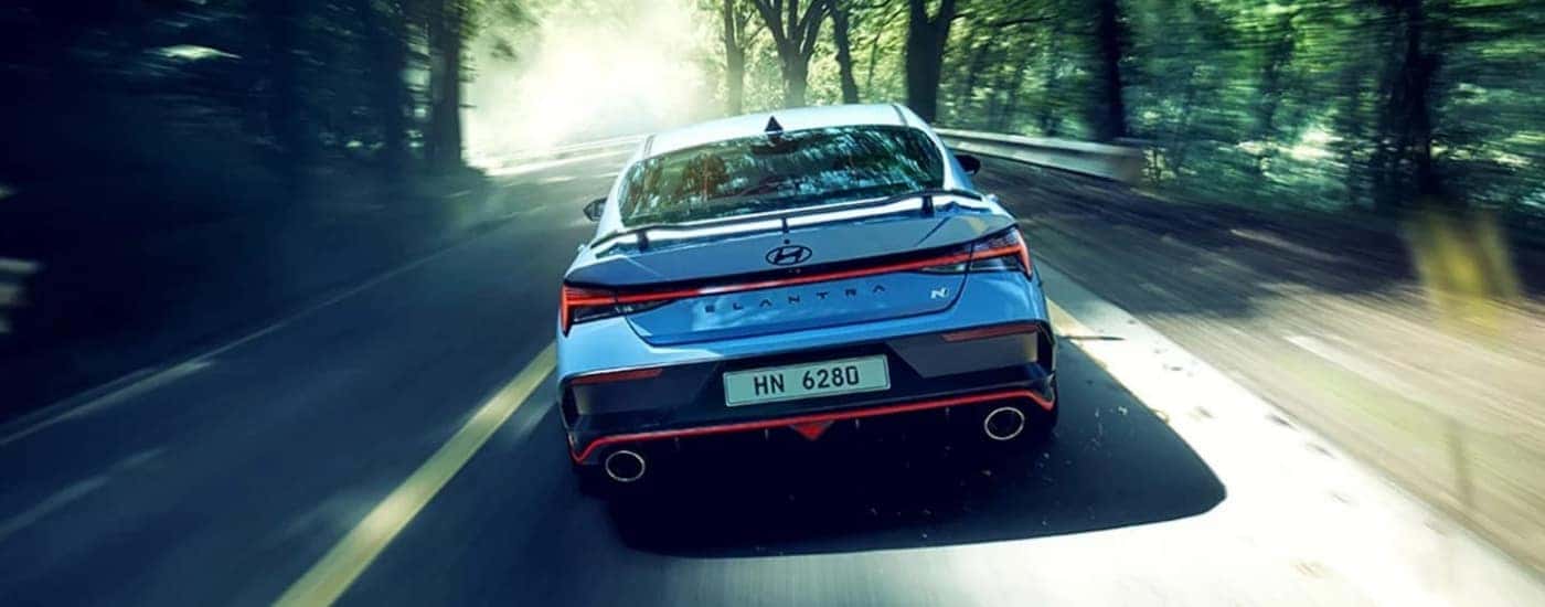 Blue 2024 Hyundai Elantra N driving on a tree-lined road
