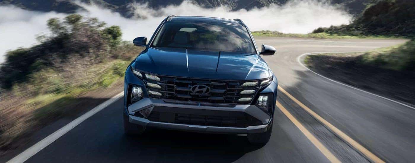 Blue 2026 Hyundai Tucson driving on a road near the coast.