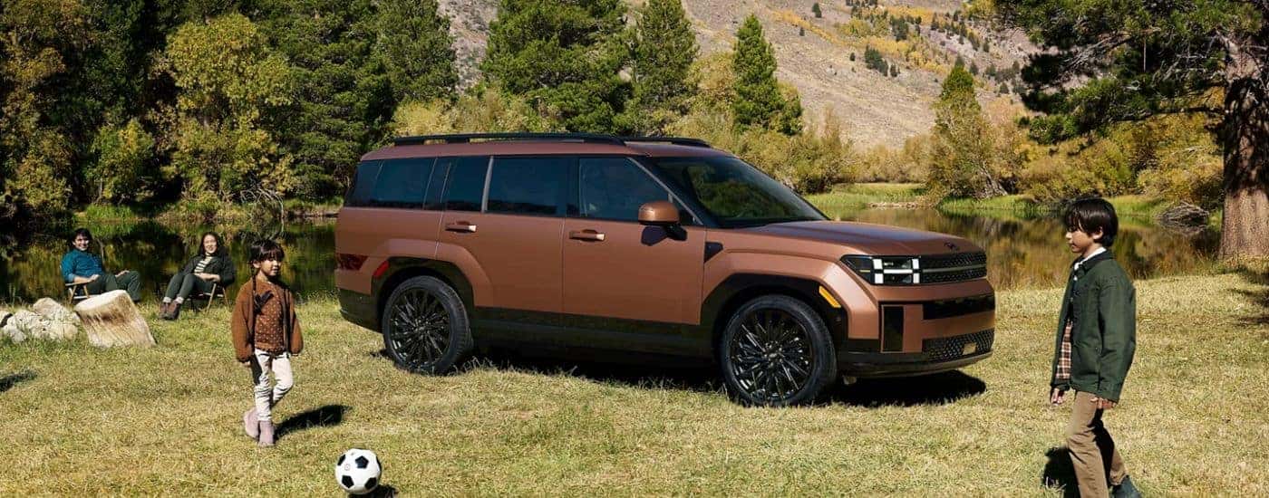 A brown 2026 Hyundai Santa Fe shown parked by a pond and family playing soccer.