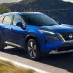 A blue 2021 Nissan Rogue is driving down a two lane road.