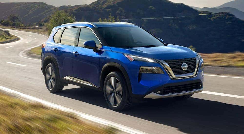 A blue 2021 Nissan Rogue is driving down a two lane road.