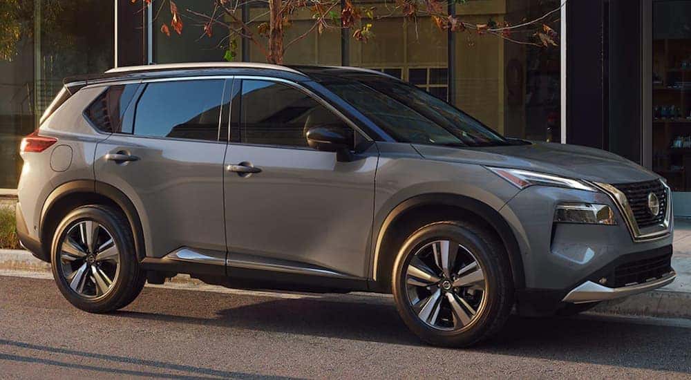A grey 2021 Nissan Rogue is shown from the side parked in front of a modern building.