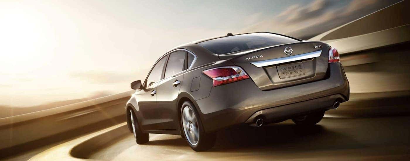A brown 2013 Nissan Altima is shown from the rear driving on a sharp corner.