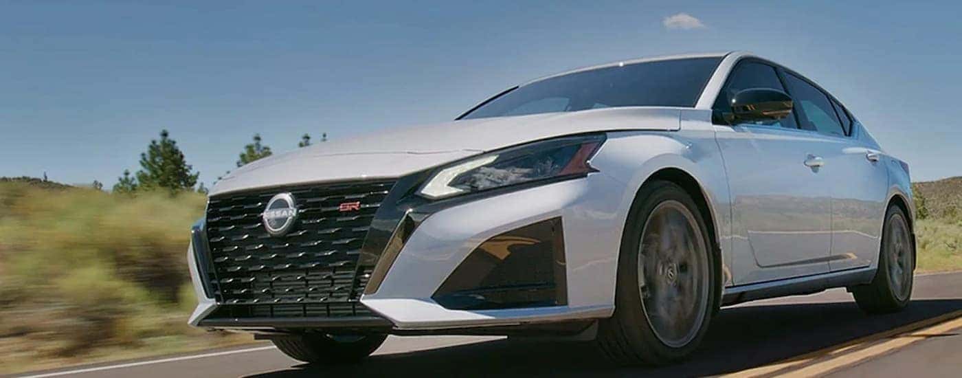 A white 2024 Nissan Altima SE is shown driving on a highway through a desert.