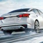 A white 2021 Nissan Altima is shown from the rear driving on a snowy road after leaving a Nissan Altima dealership.