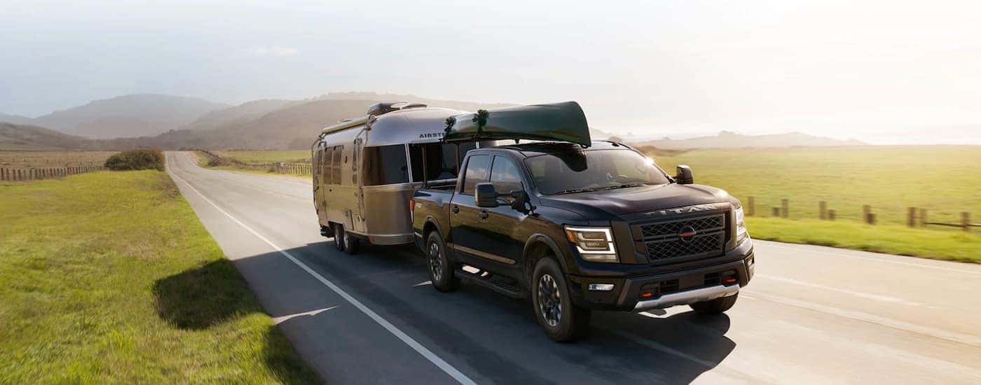 A black 2021 Nissan Titan is shown towing a trailer past a field.