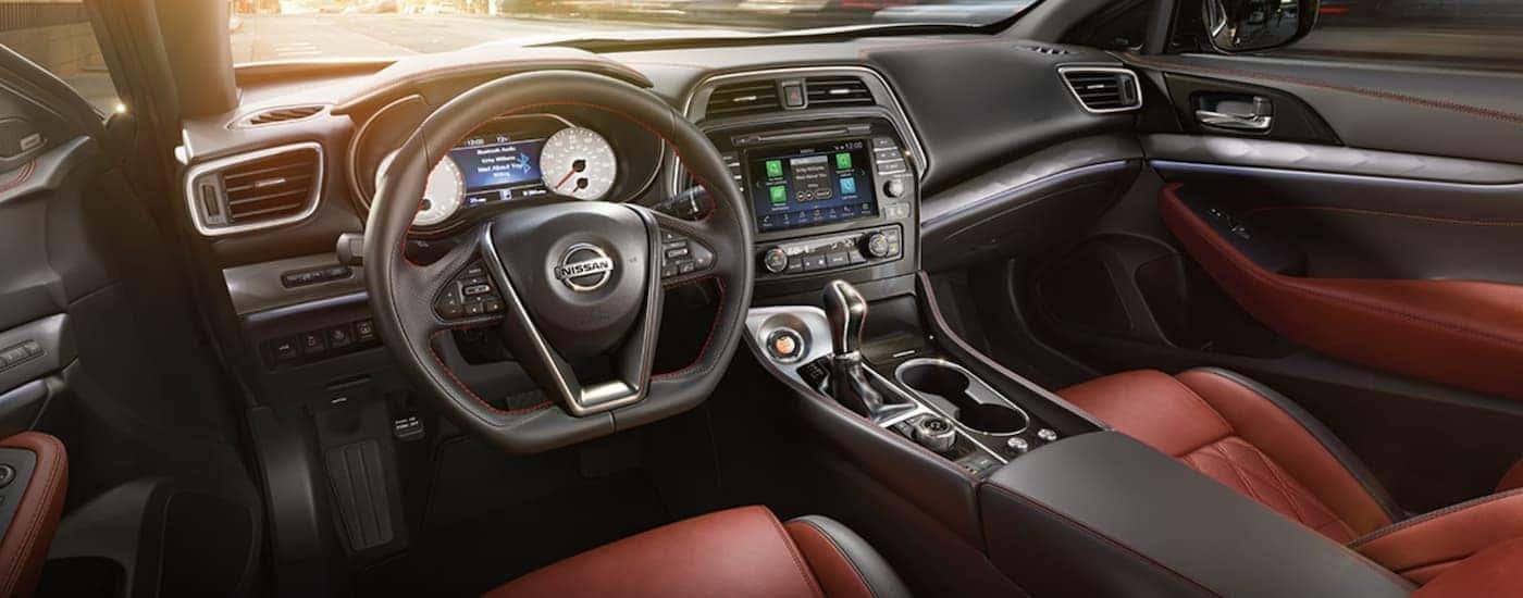 The black and red interior of a 2021 Nissan Maxima shows the steering wheel and infotainment screen.
