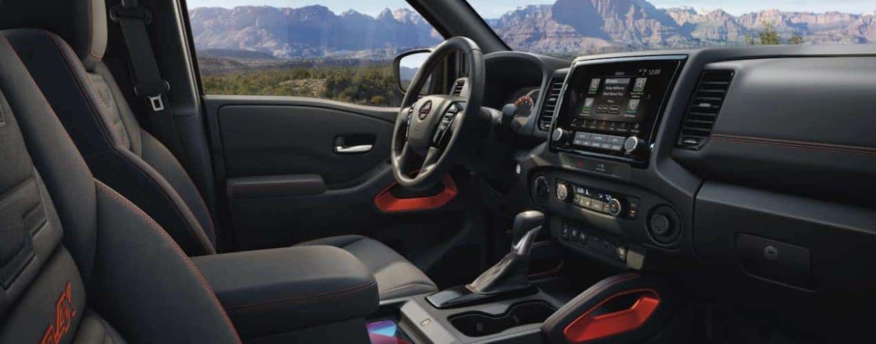 The black interior of a 2022 Nissan Frontier shows the front seat and steering wheel.