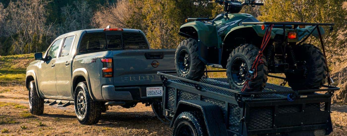 A grey 2022 Nissan Frontier is shown from the rear towing a trailer carrying an ATV.