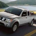 A silver 2018 Nissan Frontier is shown towing a sedan after leaving a used Nissan dealer near you.