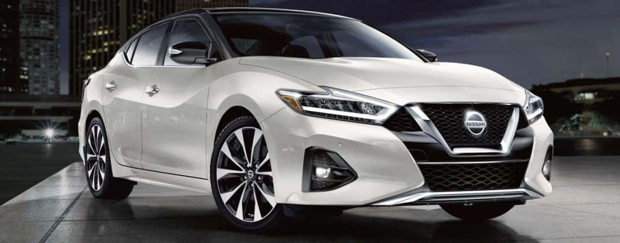 A white 2022 Nissan Maxima is shown parked in a city at night.