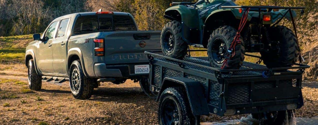 A grey 2022 Nissan Frontier PRO-4X is shown towing an ATV trailer.
