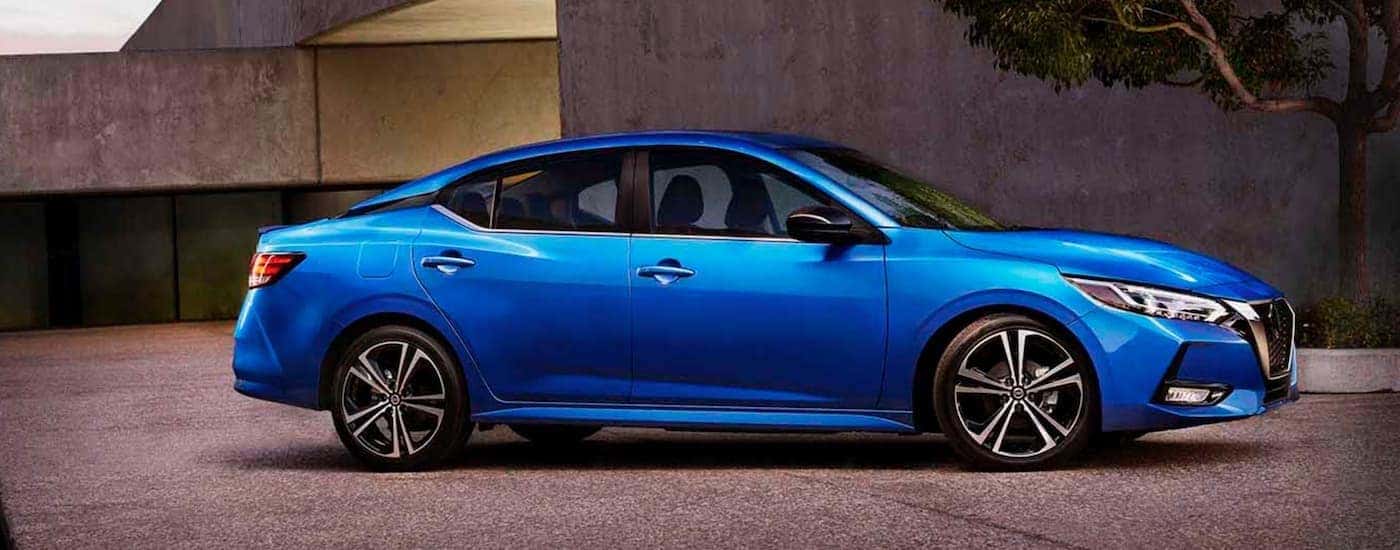 A blue 2020 Nissan Sentra is shown from the side parked in front of a building.