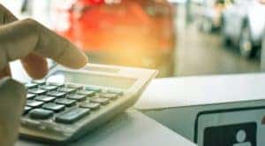 A person is shown using a calculator at a car dealership.