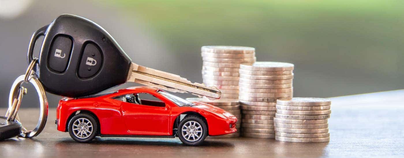 A toy car is shown in front of a pile of coins and a car key.