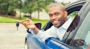A person is shown sitting in the front seat of a car holding the key out the window.