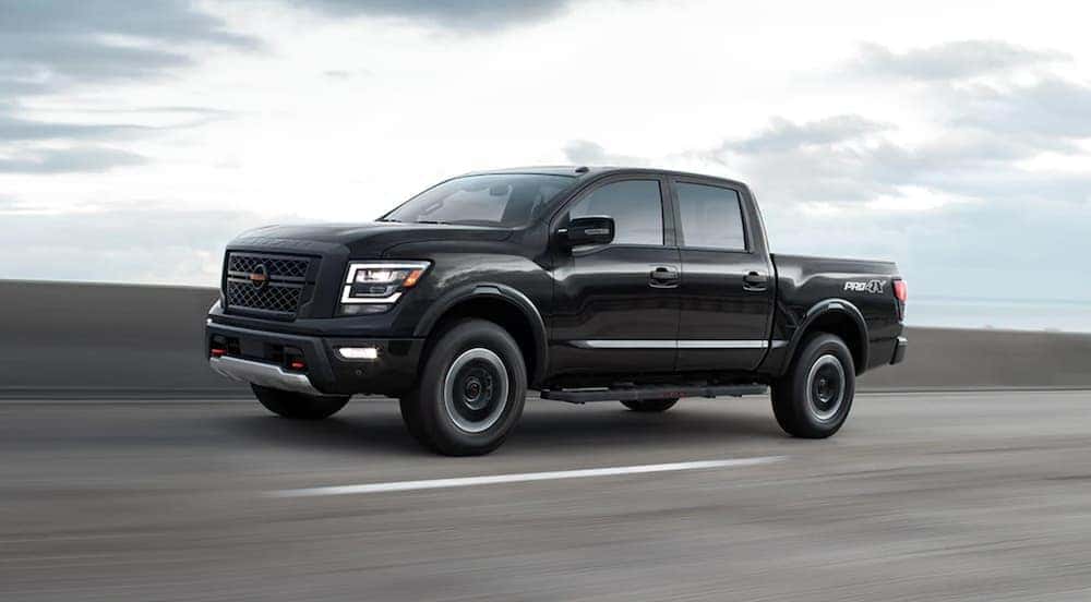 A black 2021 Nissan Titan Pro-4x is shown driving on the highway after leaving a dealer that advertises having certified used Nissan near you.
