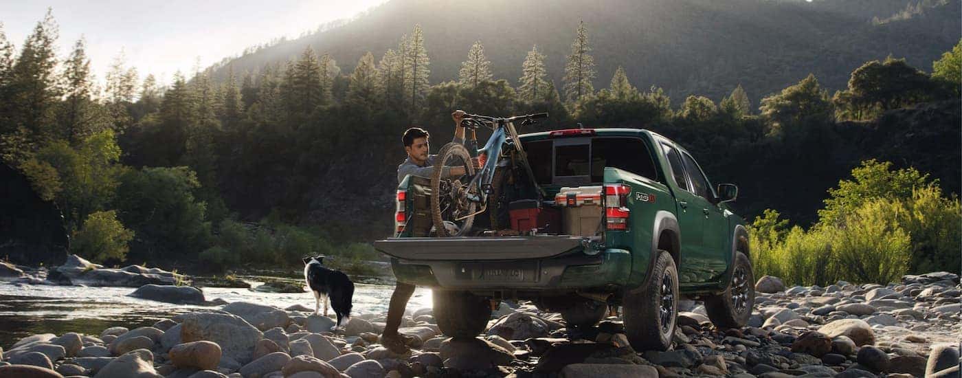 A green 2022 Nissan Frontier Pro-4X is shown from the rear parked on a rocky riverbank.