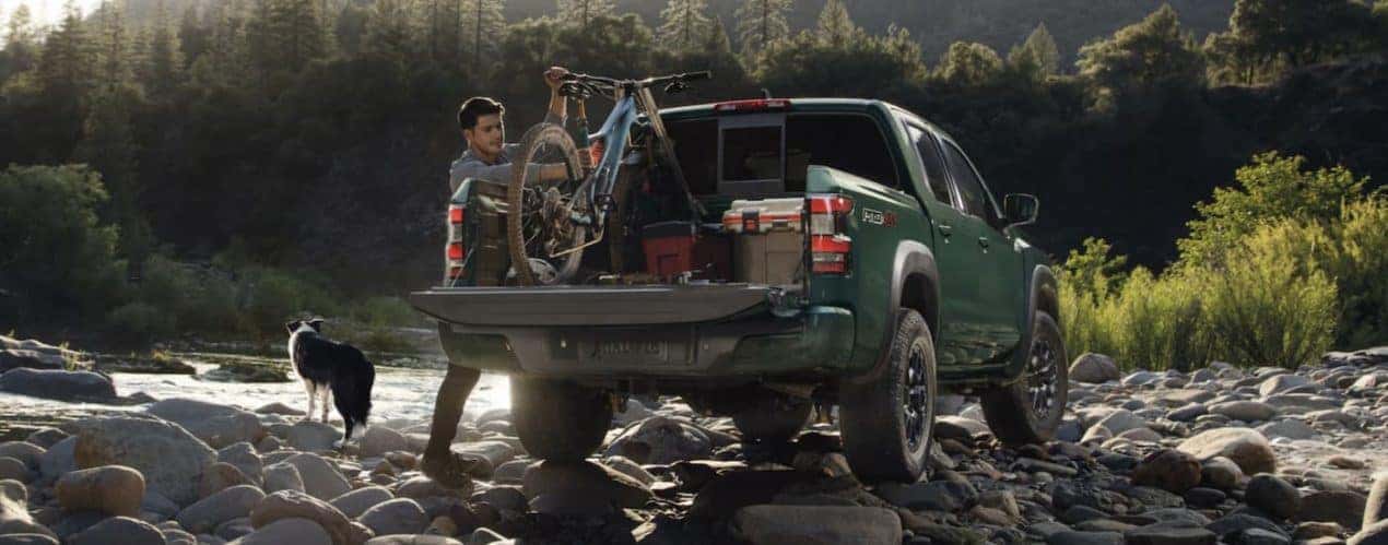 A person storing a bike in the bed of a green 2023 Nissan Frontier