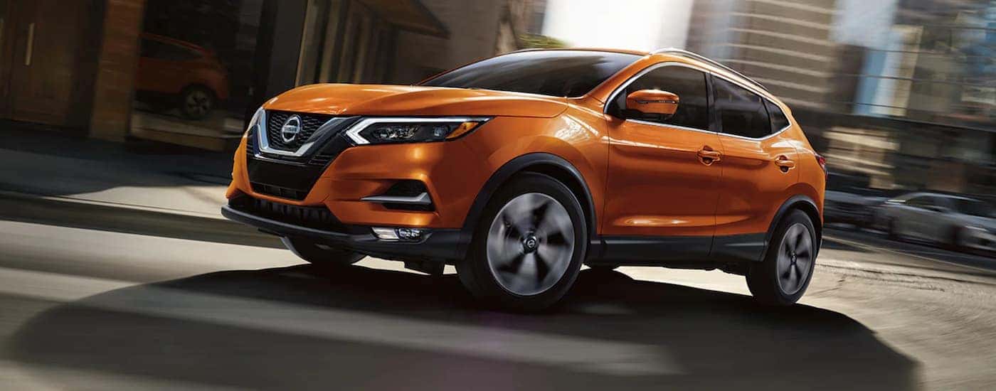 An orange 2020 Nissan Rogue Sport is shown from the side driving on a city street.