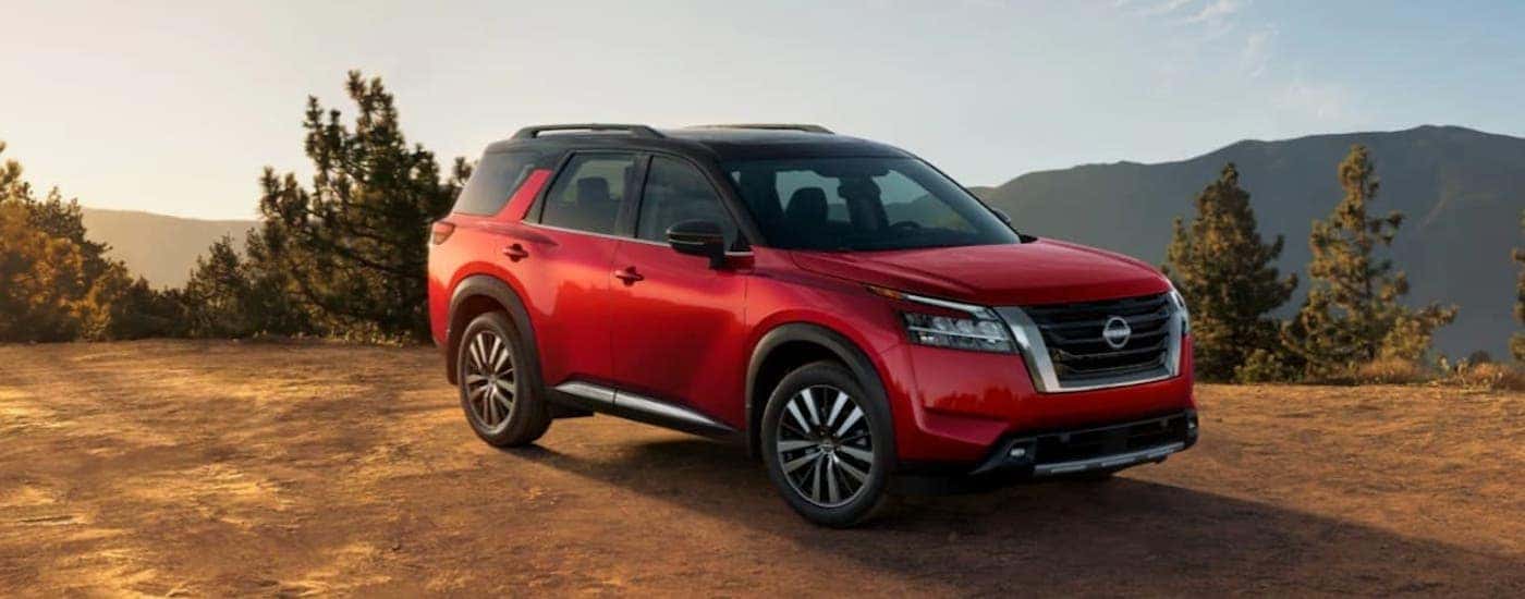 A red Nissan Pathfinder is shown parked on a dirt patch on the top of a mountain