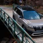 A brown 2023 Nissan Pathfinder Rock Creek is shown from the front while driving over a bridge after leaving a dealer that has a Nissan Pathfinder for sale.