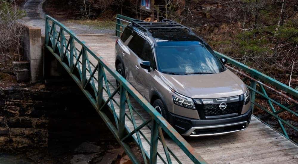 A brown 2023 Nissan Pathfinder Rock Creek is shown from the front while driving over a bridge after leaving a dealer that has a Nissan Pathfinder for sale.