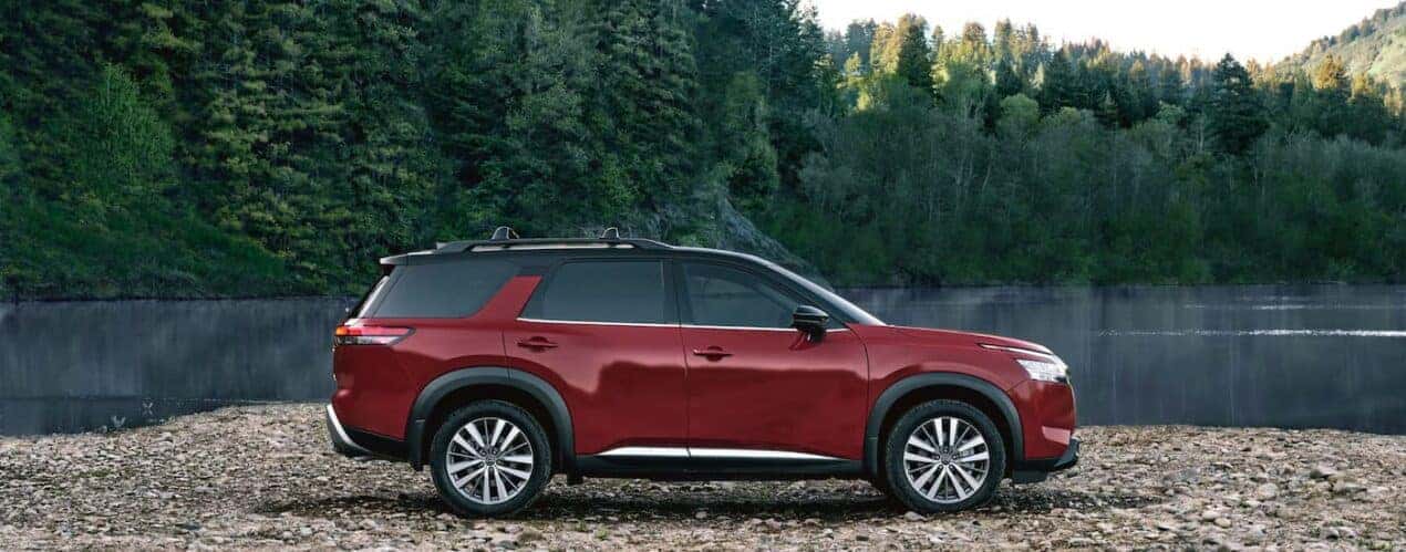 A red 2023 Nissan Pathfinder Platinum is shown from the side parked on a rocks.