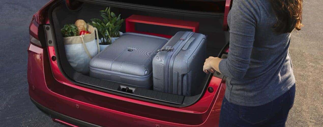 A person placing luggage into the trunk of a red 2023 Nissan Versa