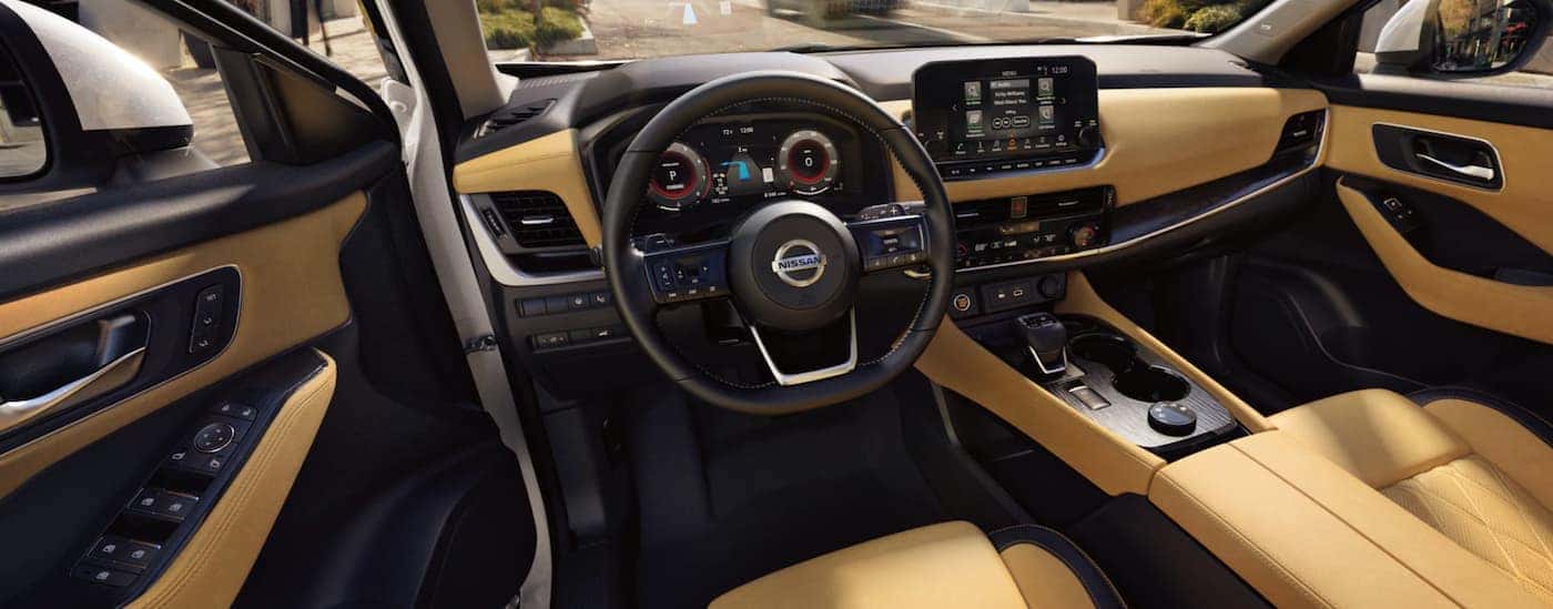 The black and yellow interior of a 2021 Nissan Rogue shows the steering wheel infotainment screen.