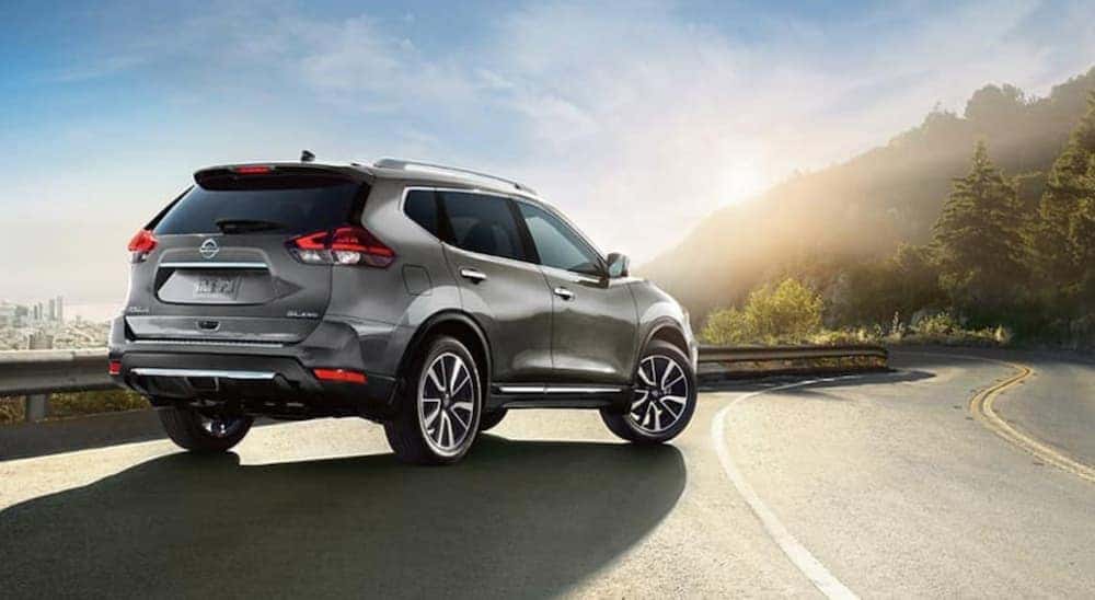 A silver 2018 Nissan Rogue is shown from the rear parked on the side of winding highway road.