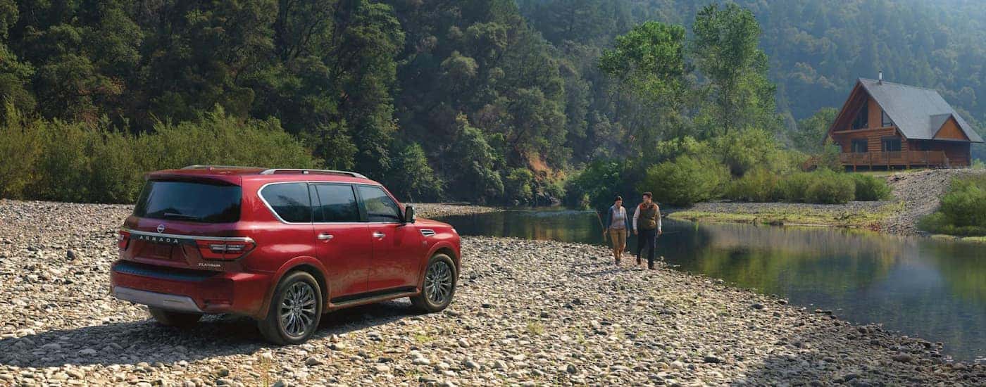 A red 2023 Nissan Armada Platinum is shown parked on rocks next to a river.