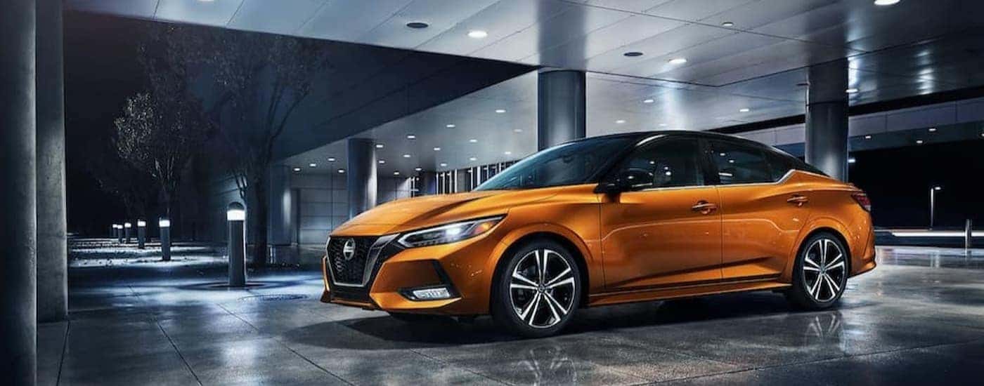An orange 2023 Nissan Sentra for sale is shown parked near a building at night.