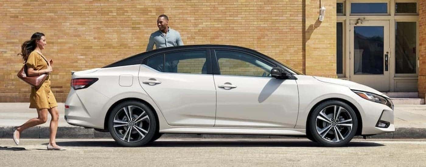 A white 2023 Nissan Sentra is shown parked near a brick building.
