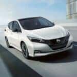 A white 2024 Nissan LEAF is shown driving on a bridge.