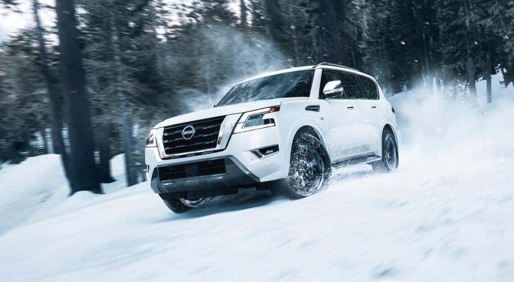 A white 2023 Nissan Armada is shown driving through a snowy forest.