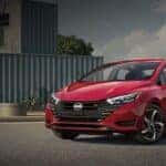 A red 2024 Nissan Versa parked in front of a modern building.