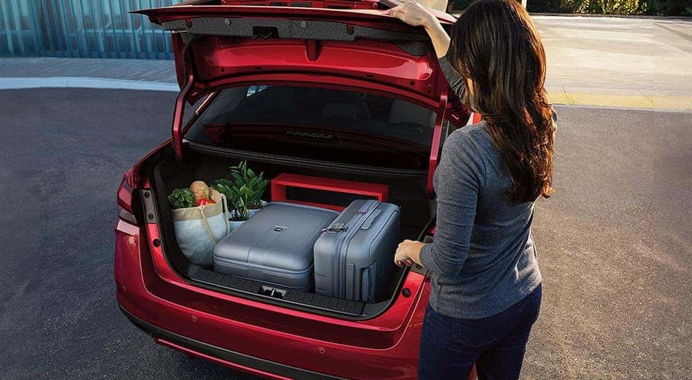 A woman loading luggage, groceries, and decor into the trunk of a red 2024 Nissan Versa.