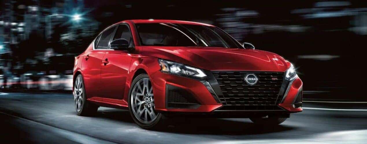 A red 2024 Nissan Altima SR is shown driving at night after a 2024 Nissan Altima vs 2024 Toyota Camr…