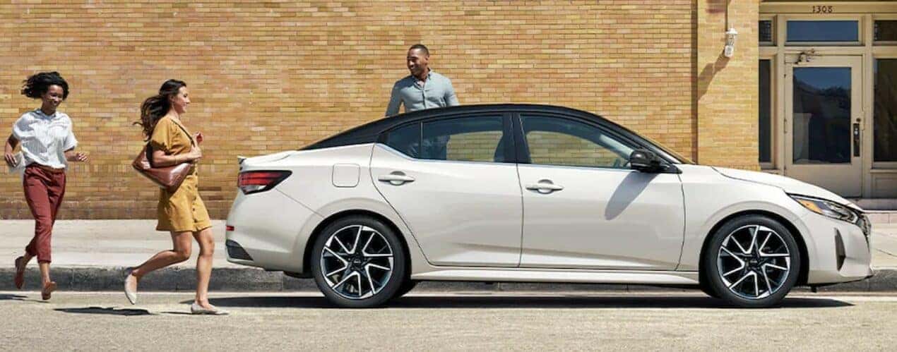 A white 2024 Nissan Sentra is shown parked near several people after a 2024 Nissan Sentra vs 2024 Kia Forte comparison.