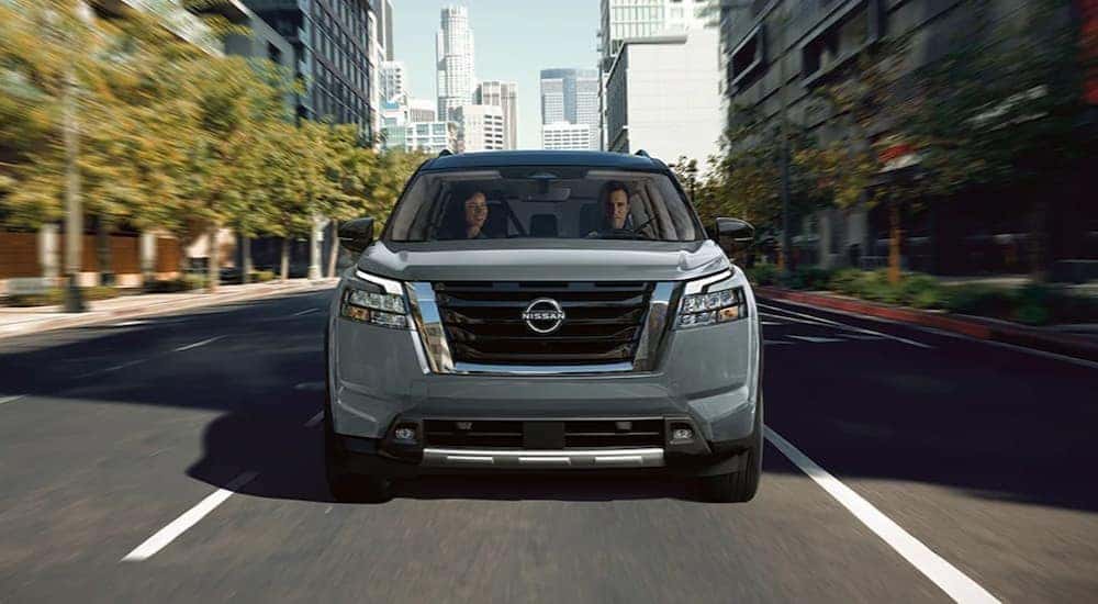 A gray 2024 Nissan Pathfinder is shown driving on a city street.