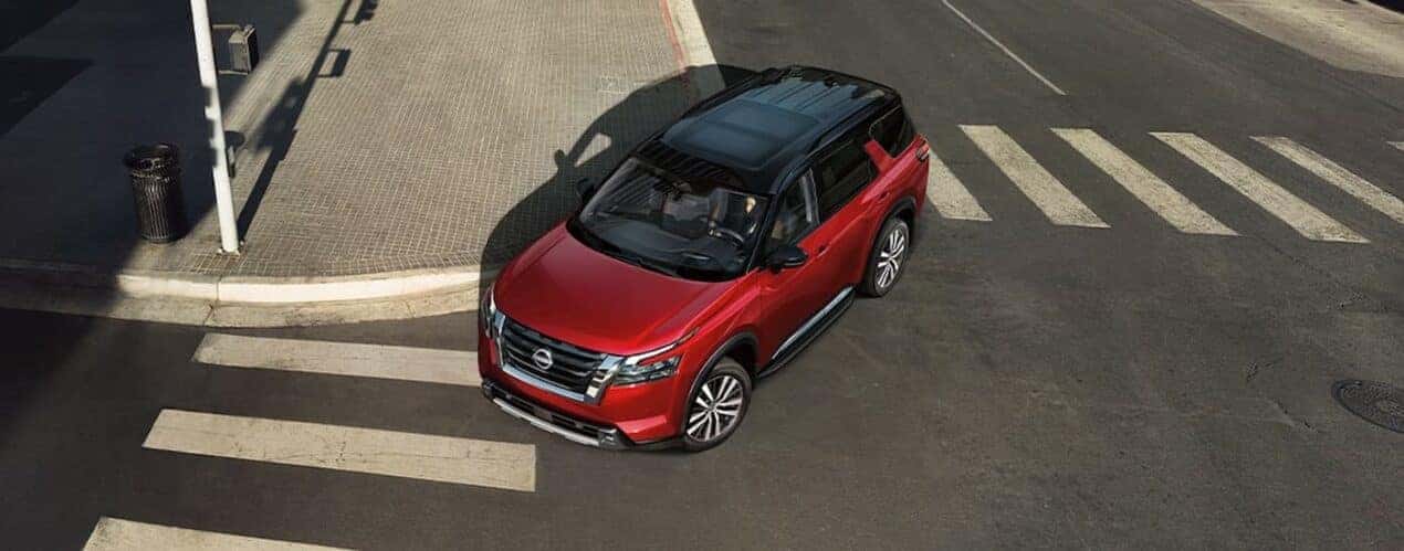 A red 2024 Nissan Pathfinder is driving on a city street.