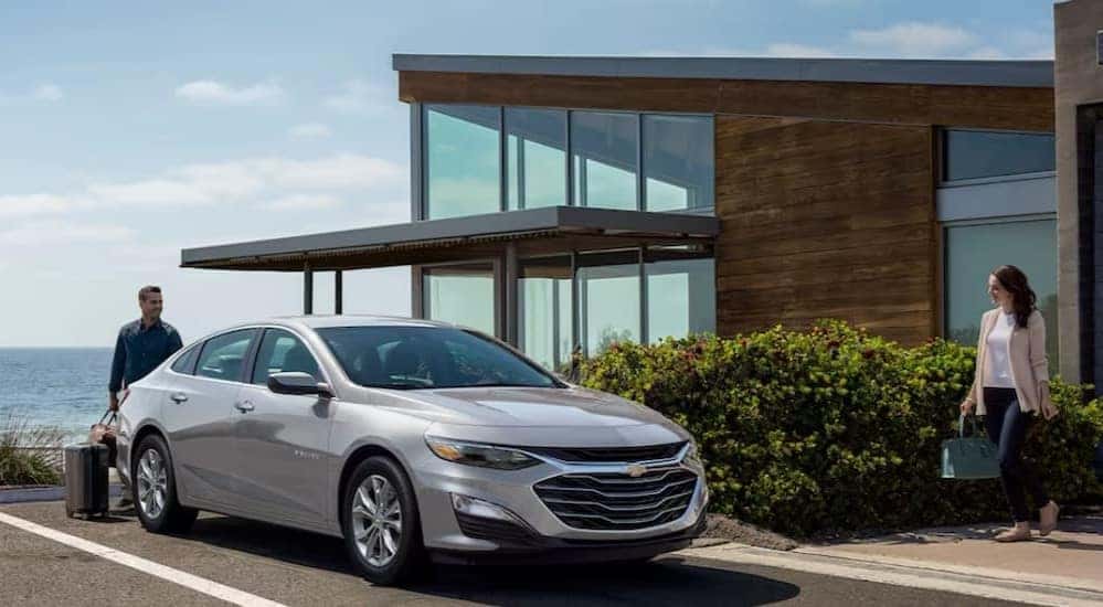 A silver 2024 Chevy Malibu is shown parked near a house.
