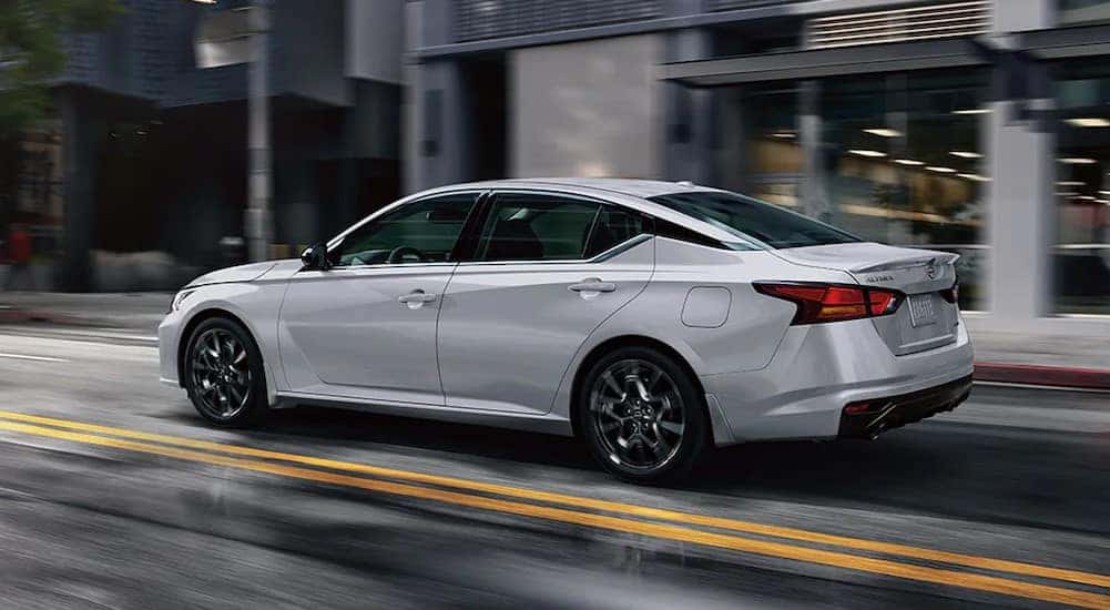 A white 2024 Nissan Altima is shown driving on a city street.